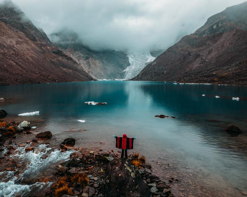 Foto panorámica de un turista con poncho andino junto a la laguna Huayna Ausangate